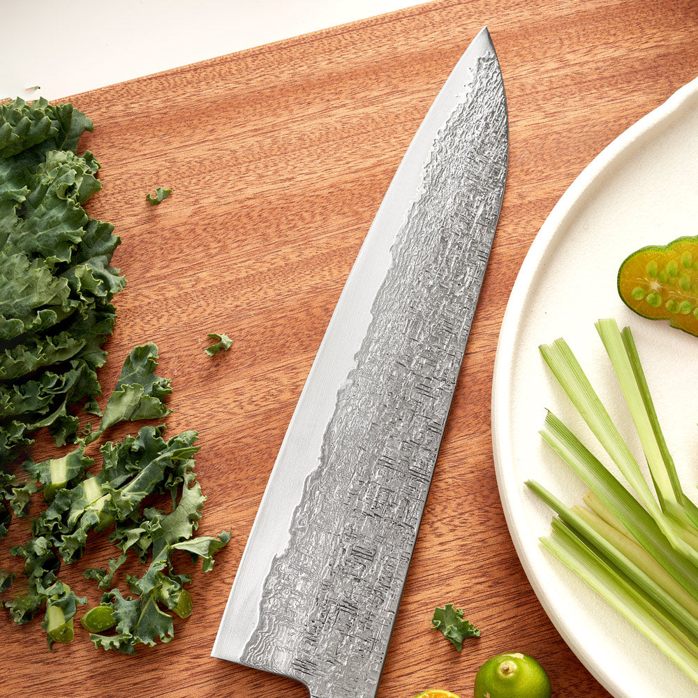 Chef's knife with a textured blade on a wooden cutting board with vegetables