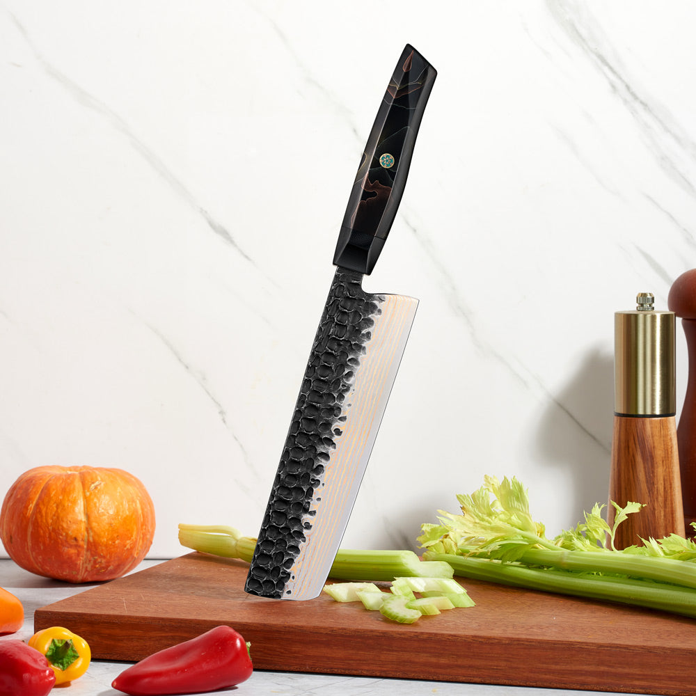 Professional vegetable Knife with a textured damascus blade on a cutting board with vegetables and a pepper grinder.