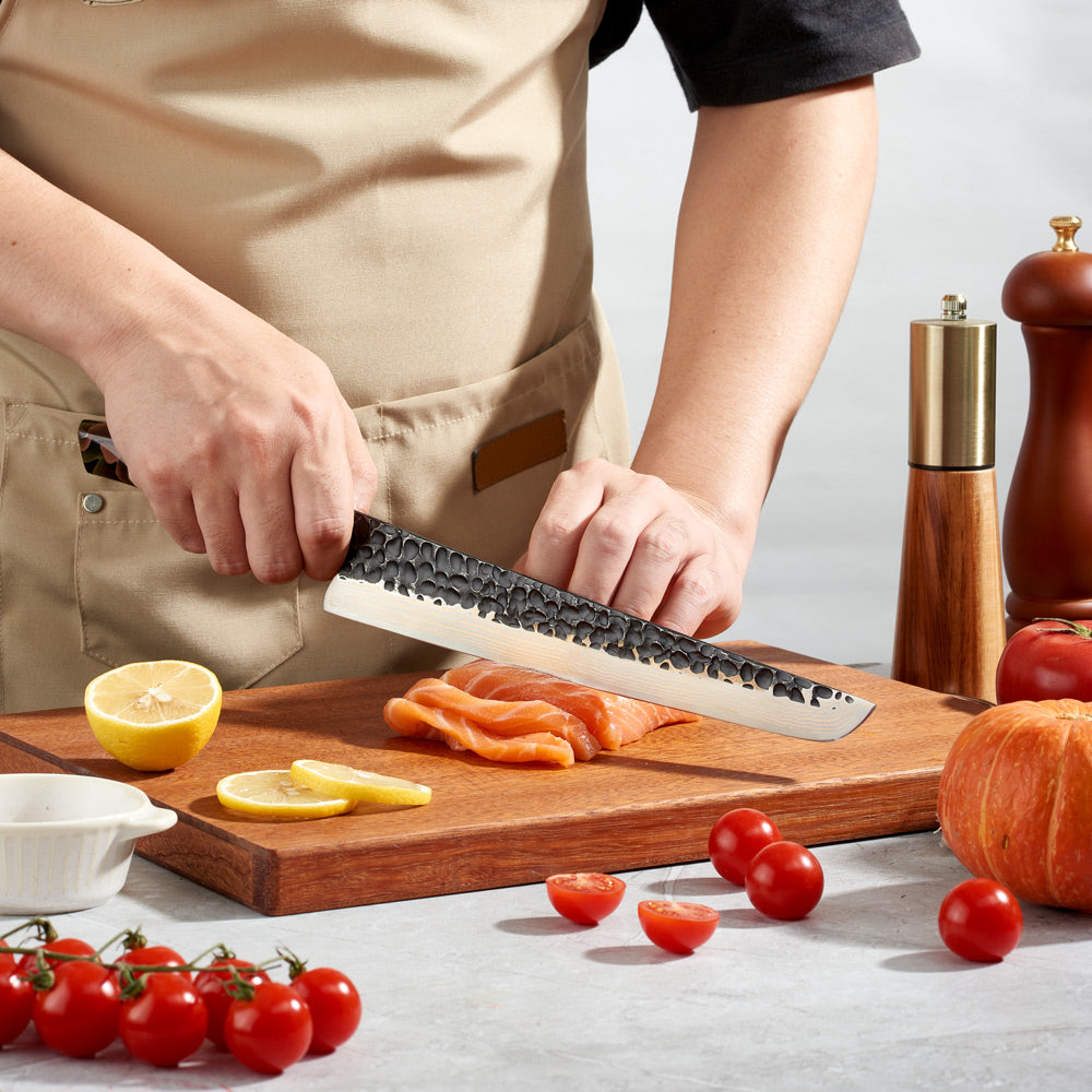 A person slicing salmon on a wooden cutting board with a Damascus and copper slicer-slaughter knife.